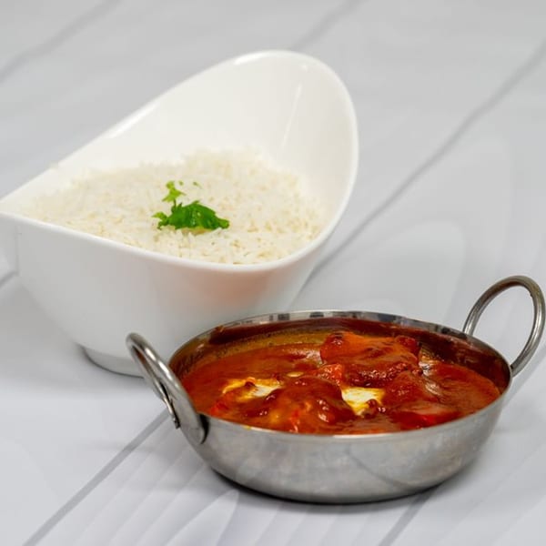 Indian butter chicken in a metal bowl with a side of white rice in a ceramic bowl.