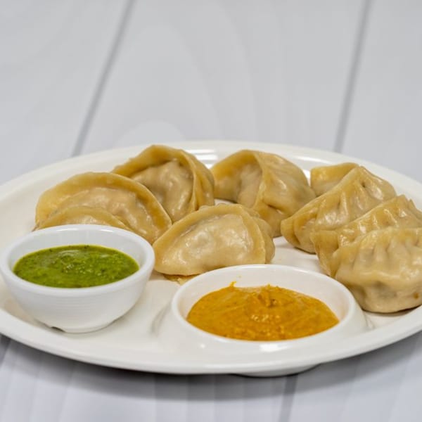 A plate of Makalu Himalayan Sherpa Restaurant's momos with green and orange dipping sauces.