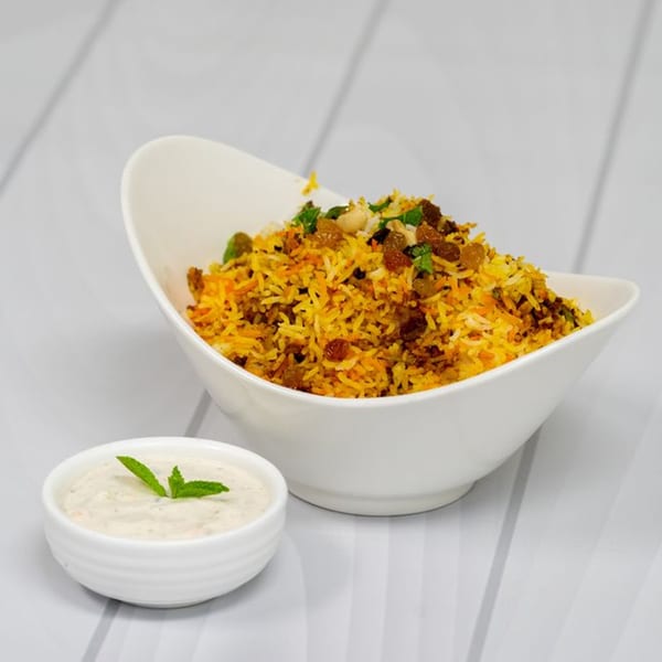 Indian biryani rice with raisins and nuts in a white bowl, with a side of raita.