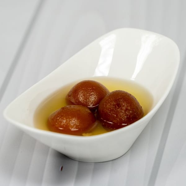 Three gulab jamun, Indian fried dough balls in syrup, in a white bowl.