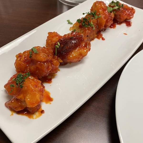 Makalu Himalayan Sherpa Restaurant's Indian-style fried chicken pieces coated in a vibrant orange sauce, garnished with herbs.